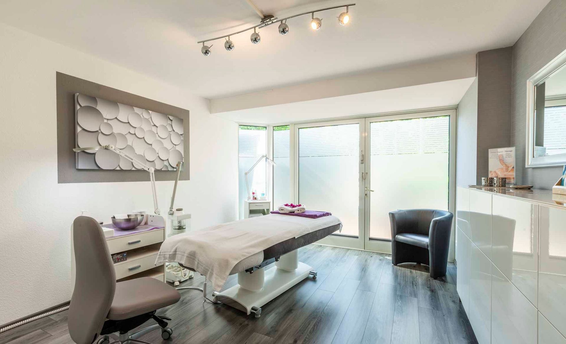 Ein Raum in der Beauty & Wellness Lounge mit einer Massageliege und einem Stuhl.