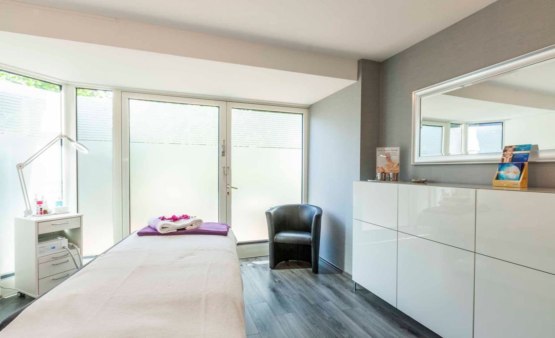 Ein Raum in der Beauty & Wellness Lounge mit einer Liege, einem Stuhl und einem Spiegel .