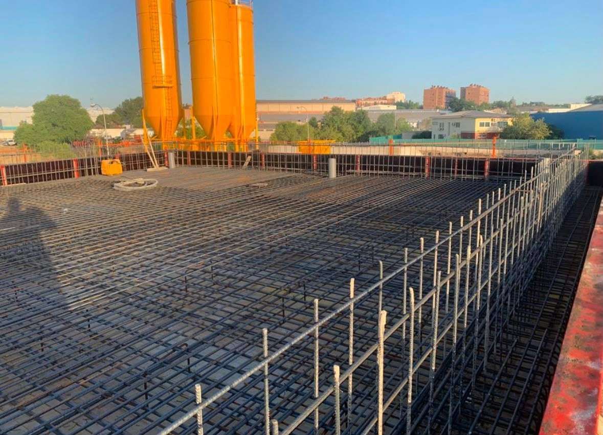Trabajadores alisando hormigón fresco en un suelo con una pala y botas.