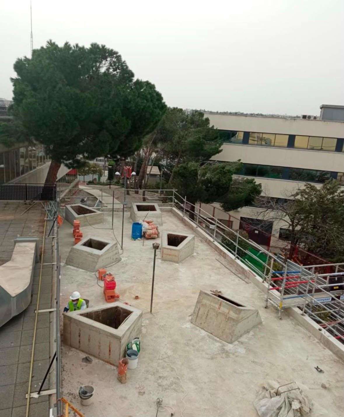 Obreros de la construcción instalan barras de refuerzo en una losa de hormigón en una obra, con maquinaria cerca.