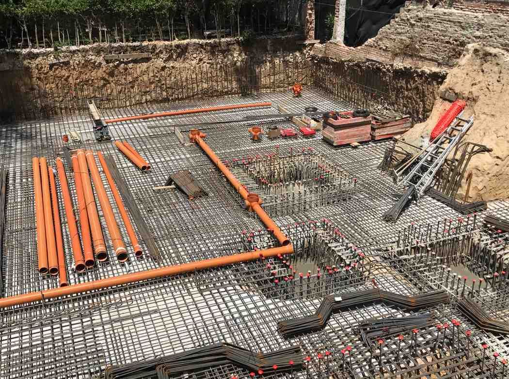 Estructura de hormigón parcialmente construida con columnas verticales en un claro boscoso bajo el cielo azul.