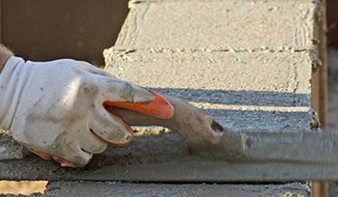 Mano enguantada que utiliza una llana para alisar el hormigón fresco a lo largo de un muro de bloques.
