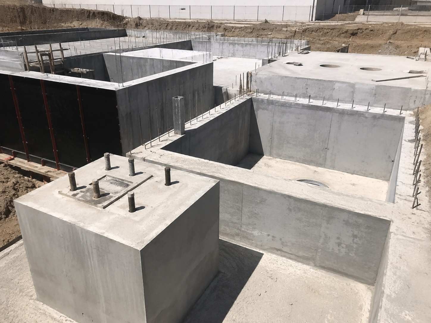 Muros de cimentación y pilares de hormigón en una obra de construcción bajo la luz del día.