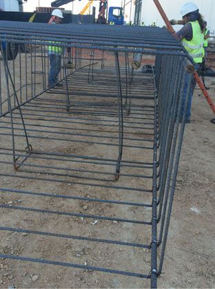 Jaula de varillas de refuerzo en construcción con un trabajador con chaleco de seguridad de color neón y casco a su lado.