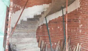 Escalera de hormigón parcialmente construida dentro de una estructura de ladrillo rojo con andamios de construcción.