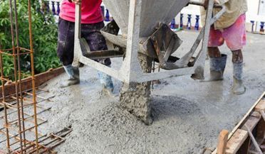 Obreros vertiendo hormigón fresco desde una hormigonera sobre una losa de construcción con barras de refuerzo en los bordes.