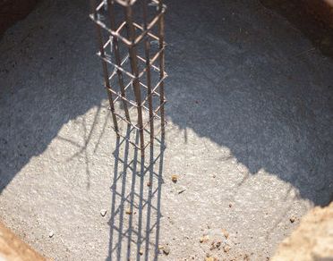 Primer plano de una jaula de barras de refuerzo vertical en un agujero de cimentación de hormigón, iluminada por la luz del sol.
