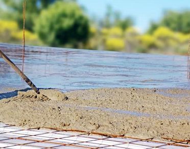 Hormigón fresco extendido y nivelado sobre una rejilla de barras de refuerzo al aire libre.