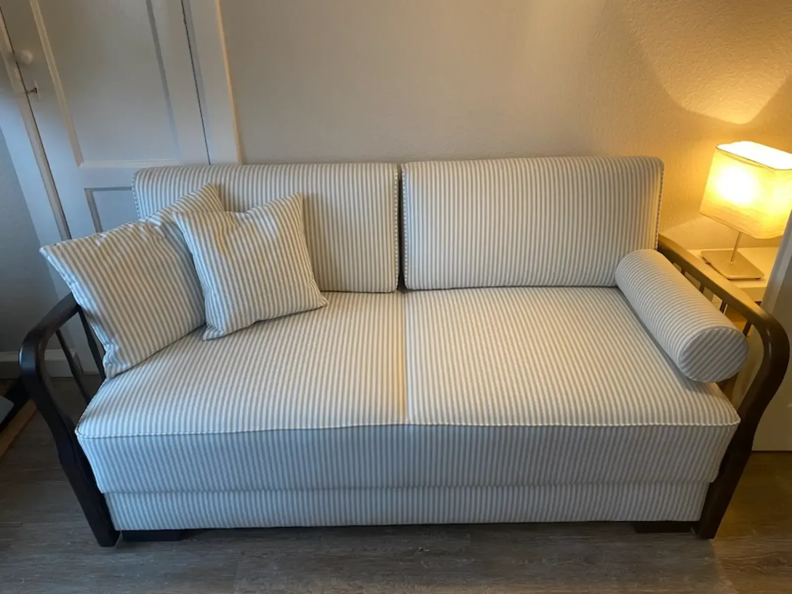 Sofa mit hellblau-weiß gestreiftem Stoffbezug, dunklem Holzrahmen und zwei Kissen in einem Zimmer mit einer Lampe.
