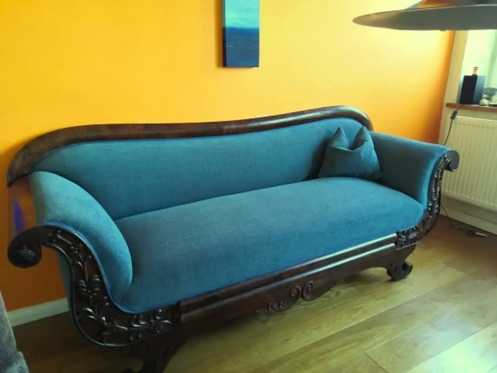 Ein blau gepolstertes antikes Sofa vor einer orangefarbenen Wand mit Holzleisten.