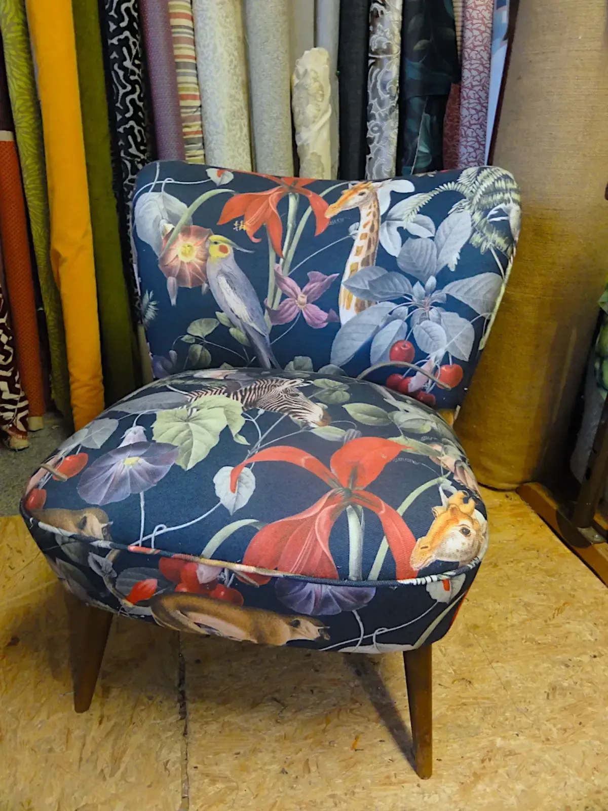 Gepolsterter Stuhl mit dunklem Blumenmuster, Vögeln und Tieren; aufgestellt in einem Stoffgeschäft.