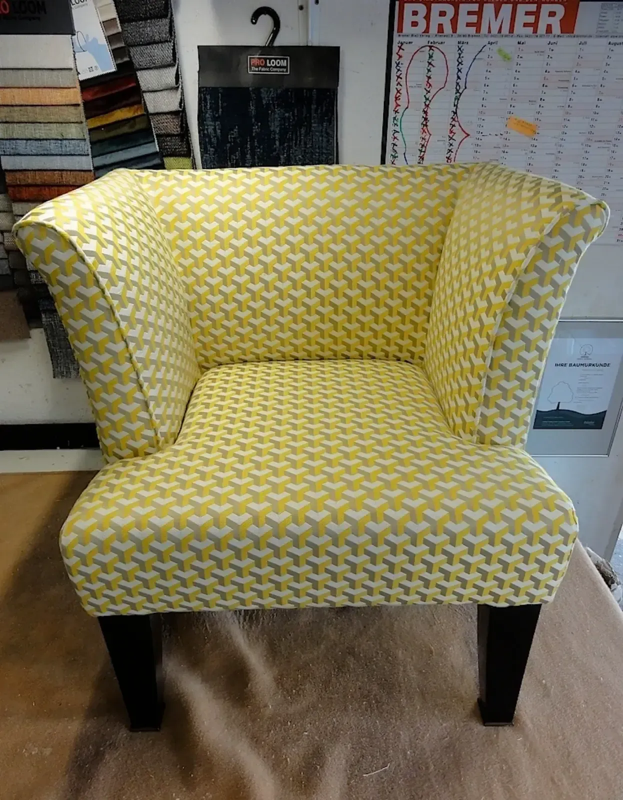 Gelb-grau gemusterter Sessel mit schwarzen Beinen.