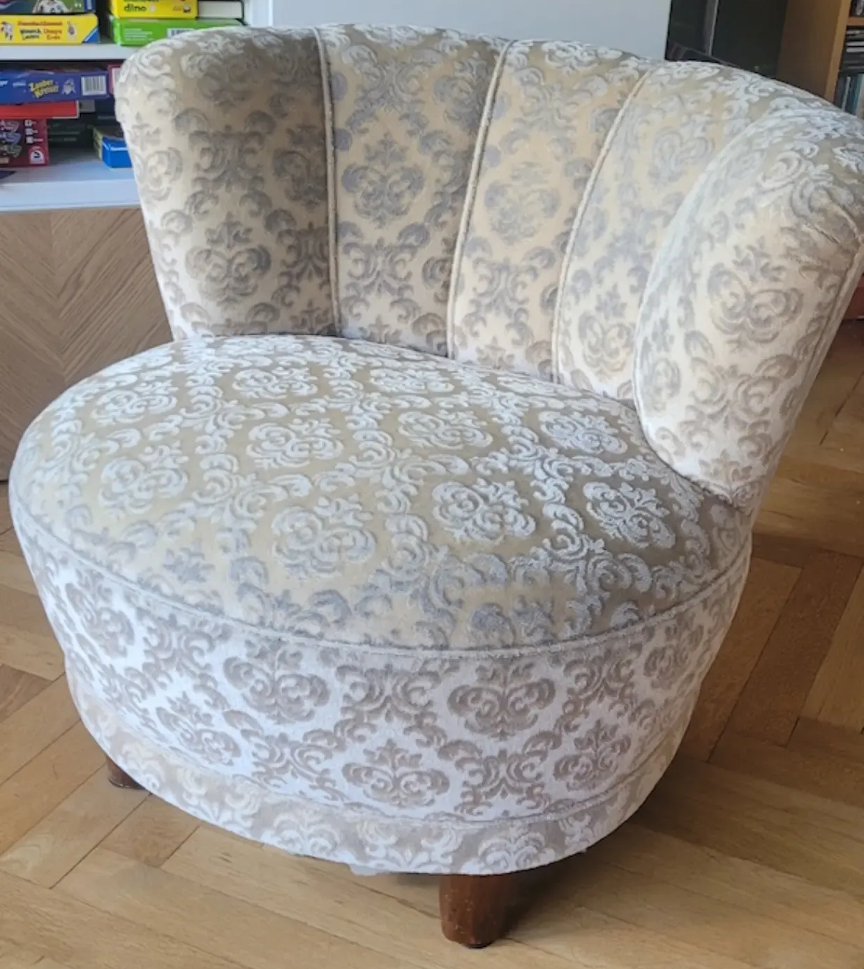 Gepolsterter Akzentstuhl mit floralem Muster in Creme- und Grautönen. Geschwungene Rückenlehne und Sitzfläche, Holzbeine.