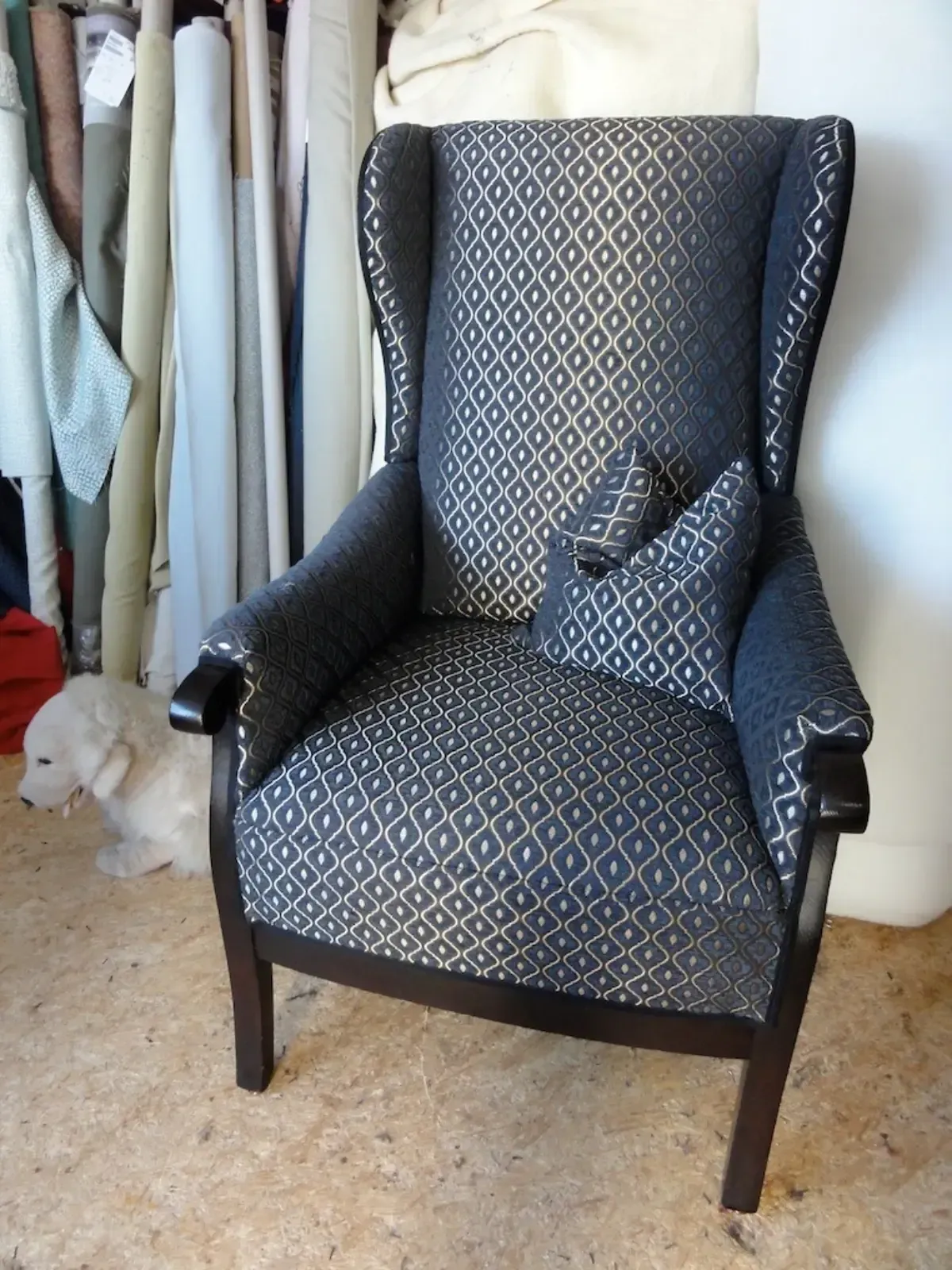 Ohrensessel mit dunkelblau gemustertem Stoffbezug, passendem Kissen und braunem Holzgestell. Ein Hund sitzt daneben.