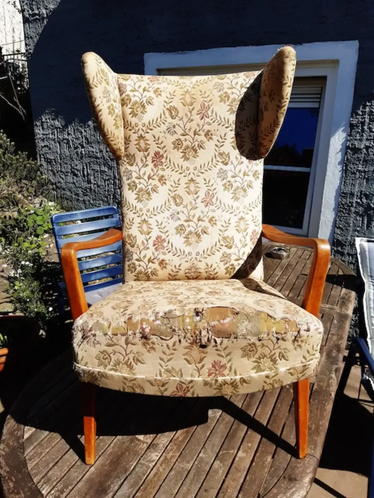 Hellbrauner Sessel mit Blumenmuster und Holzgestell auf einem Holztisch.