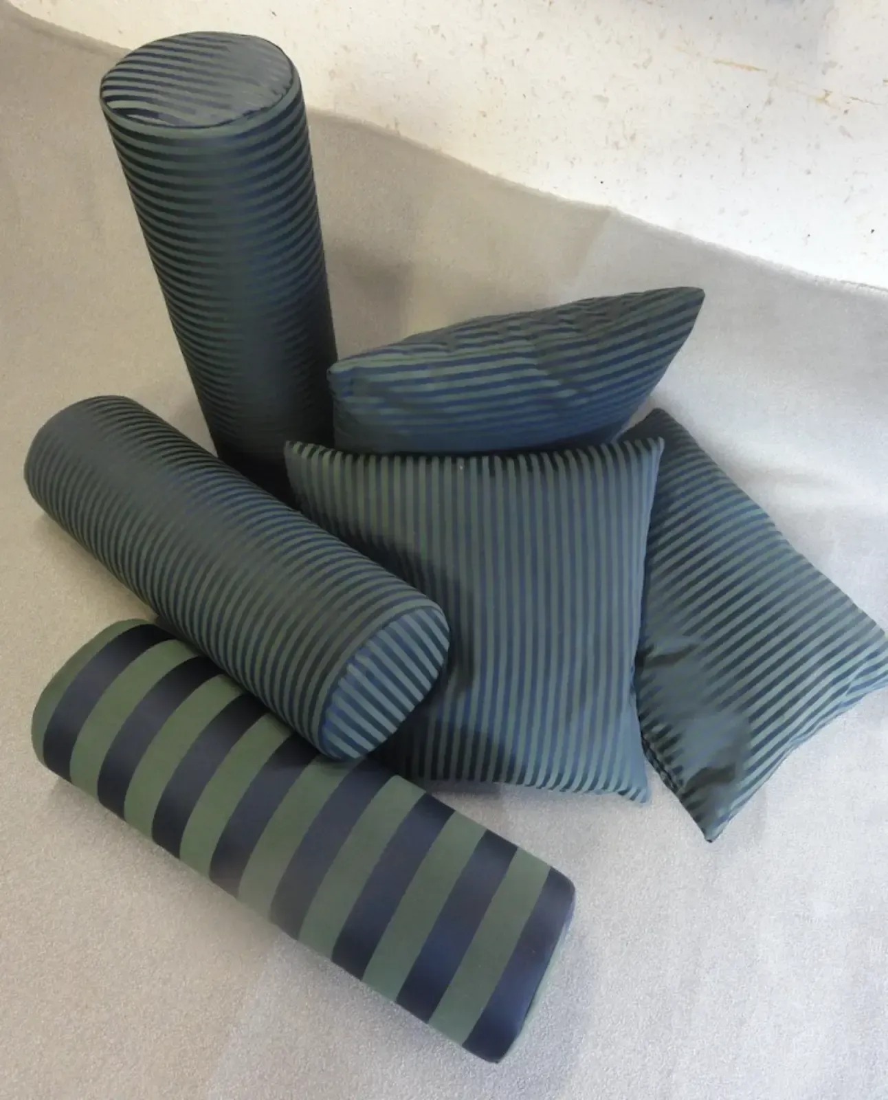 Mehrere türkis-grün gestreifte Zierkissen in verschiedenen Formen auf weißem Untergrund.