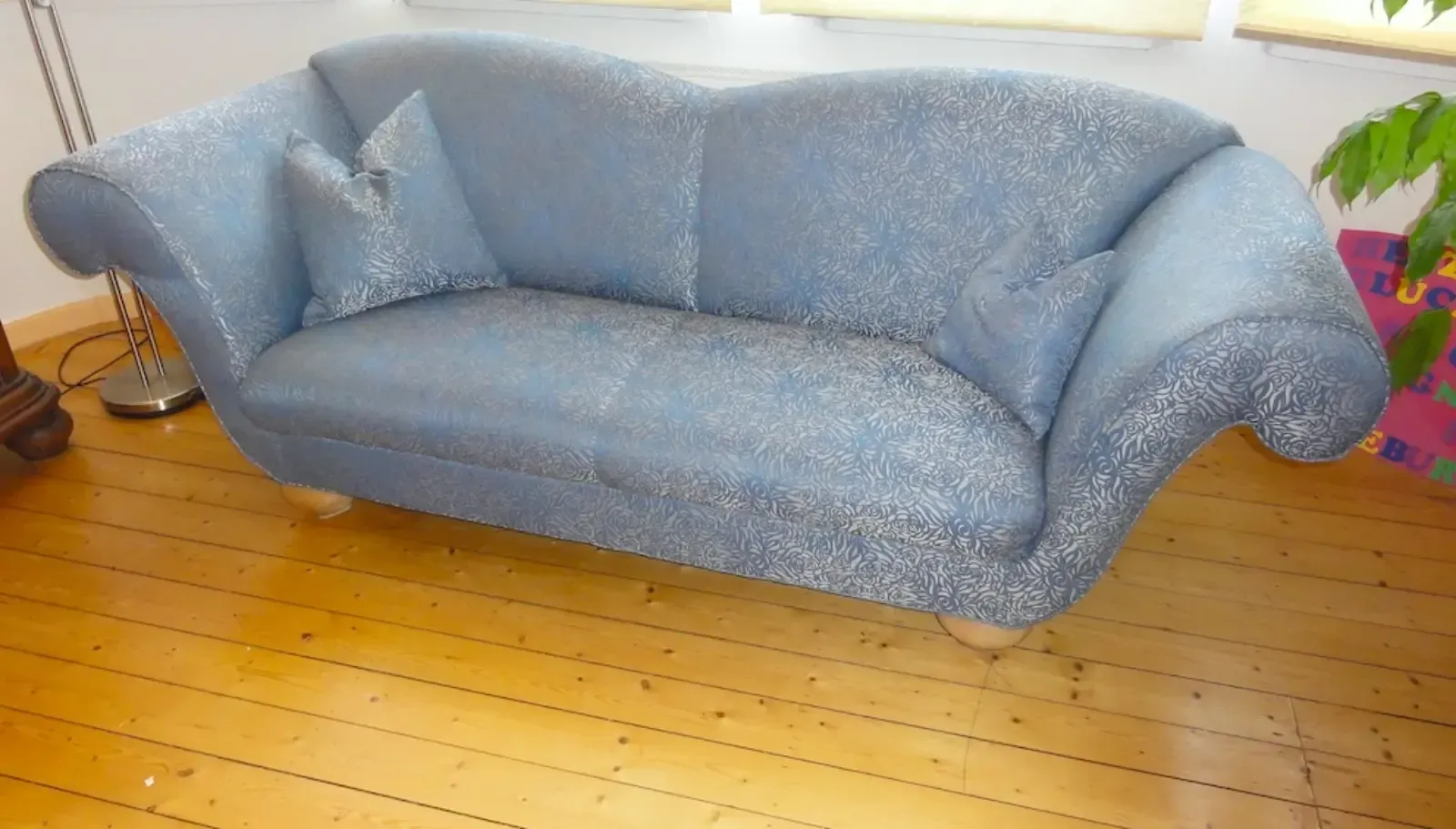 Blau gepolstertes Zweisitzer-Sofa mit zwei passenden Kissen auf einem Holzboden.
