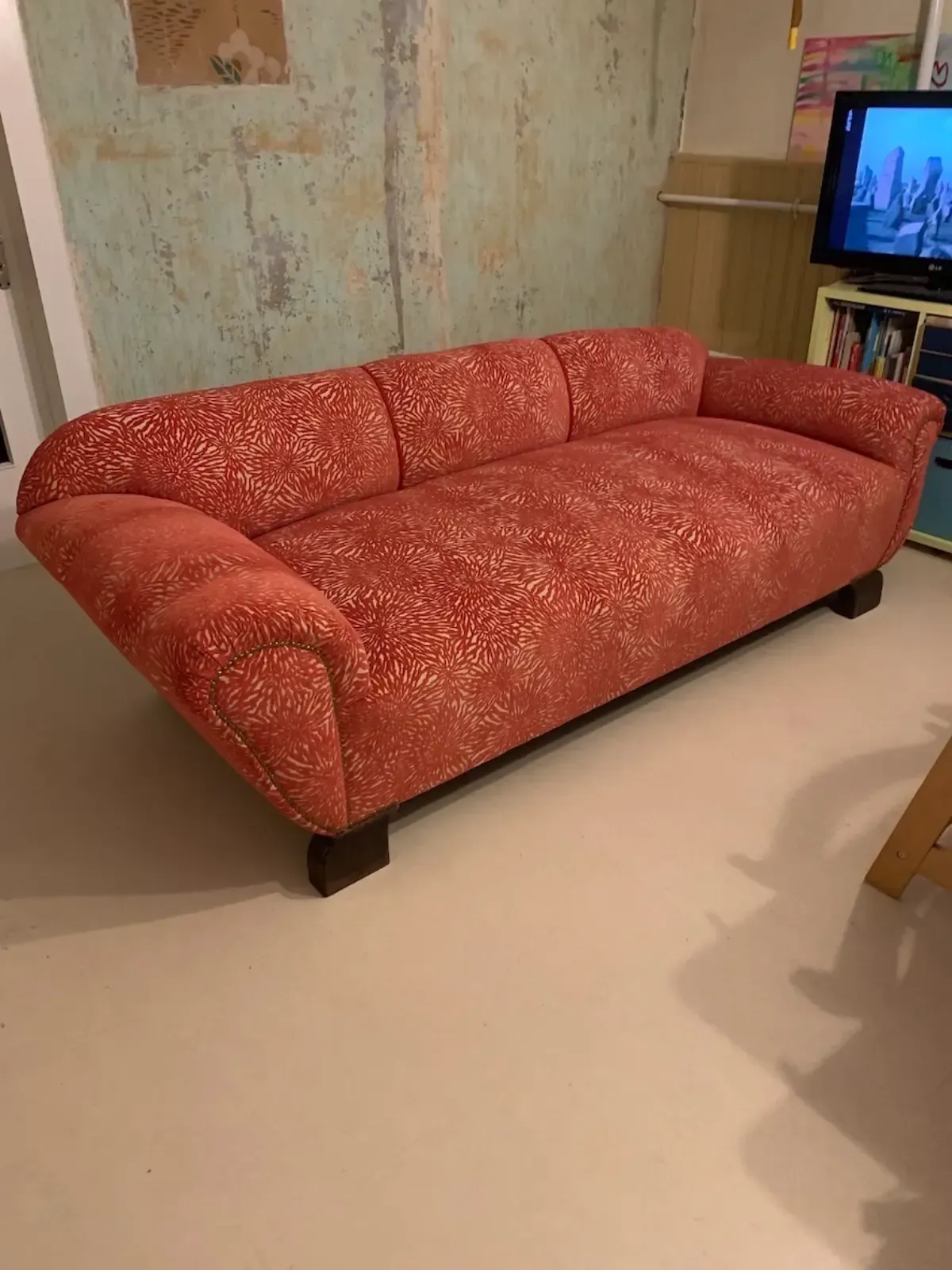 Ein rot gemustertes Sofa in einem Zimmer mit hellem Boden und abgenutzter Wand.