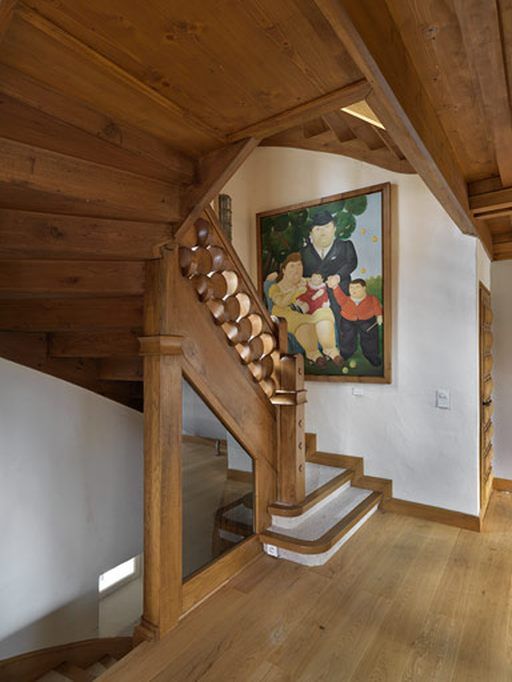 Escalier en bois avec une rampe sculptée dans une maison lumineuse, à côté d’un tableau coloré encadré.
