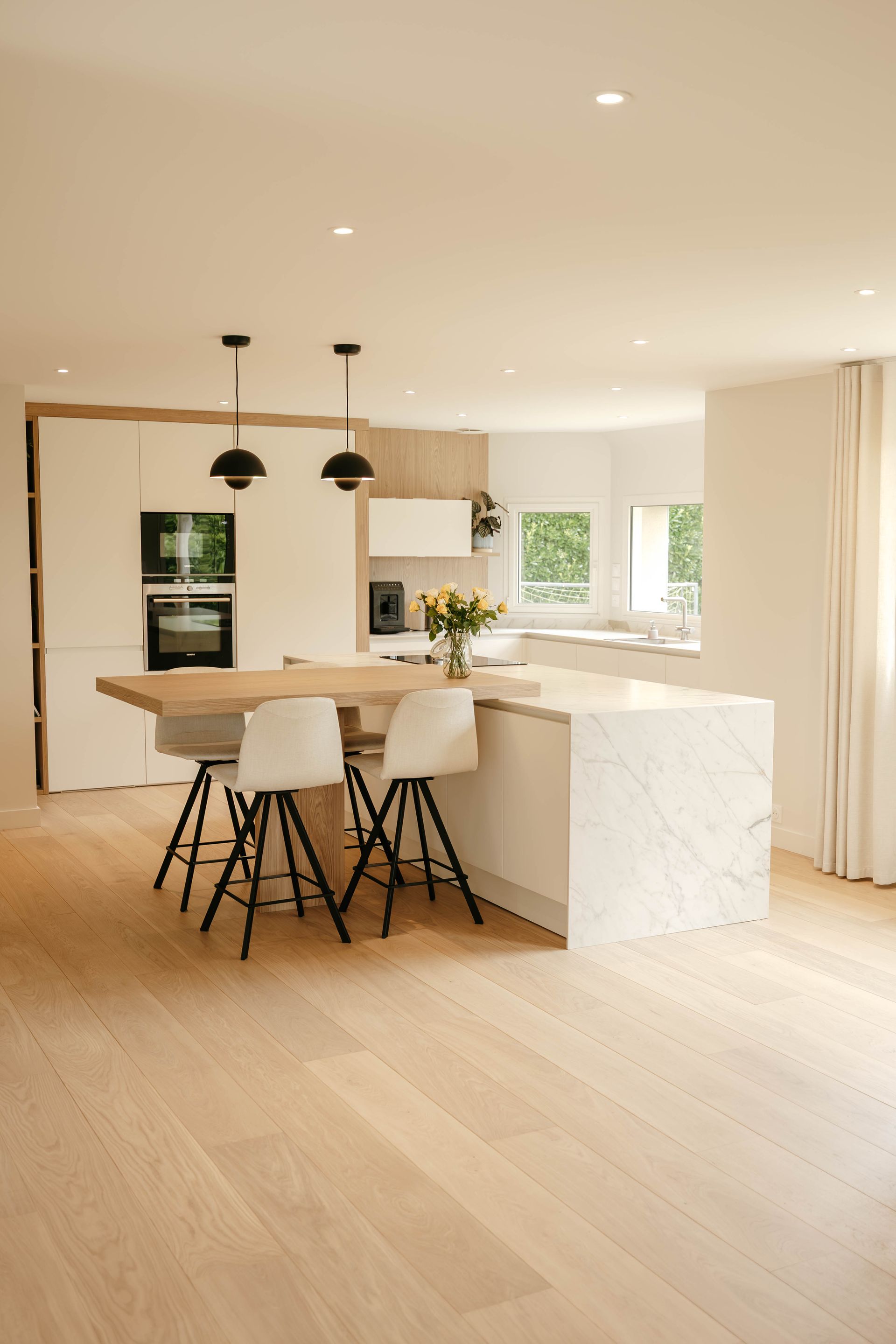 Cuisine lumineuse et moderne avec un îlot en marbre blanc, un parquet en bois et des suspensions noires