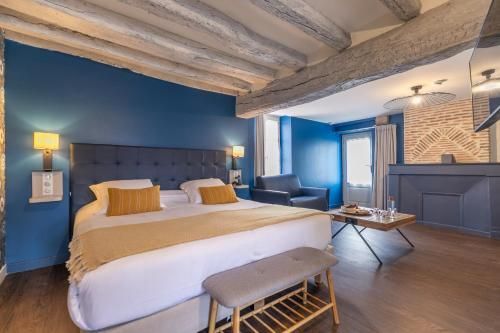 Chambre moderne aux murs bleus, avec un lit blanc, des poutres en bois et un coin salon près de la fenêtre