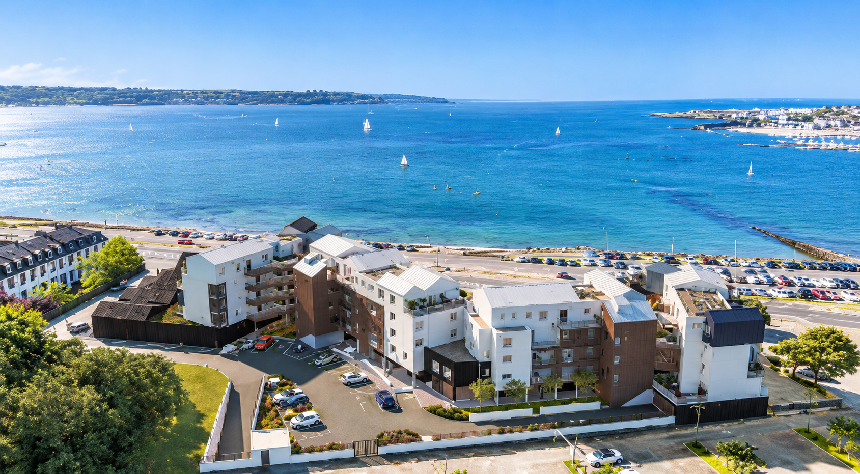 Immeubles résidentiels en bord de mer donnant sur une baie d’un bleu éclatant, avec des voiliers et une plage de sable