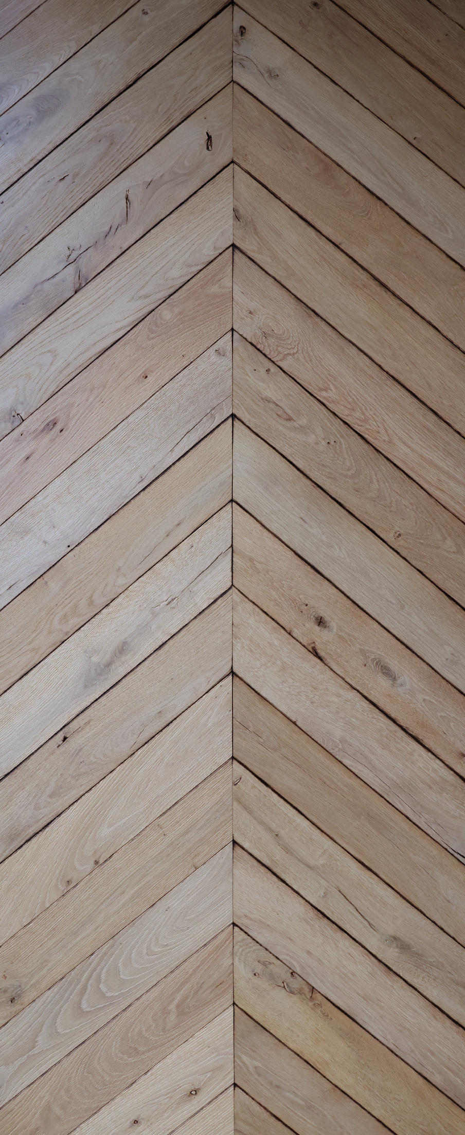 Des lames de bois clair à motif chevron se rejoignent dans un angle, formant une jointure en V.