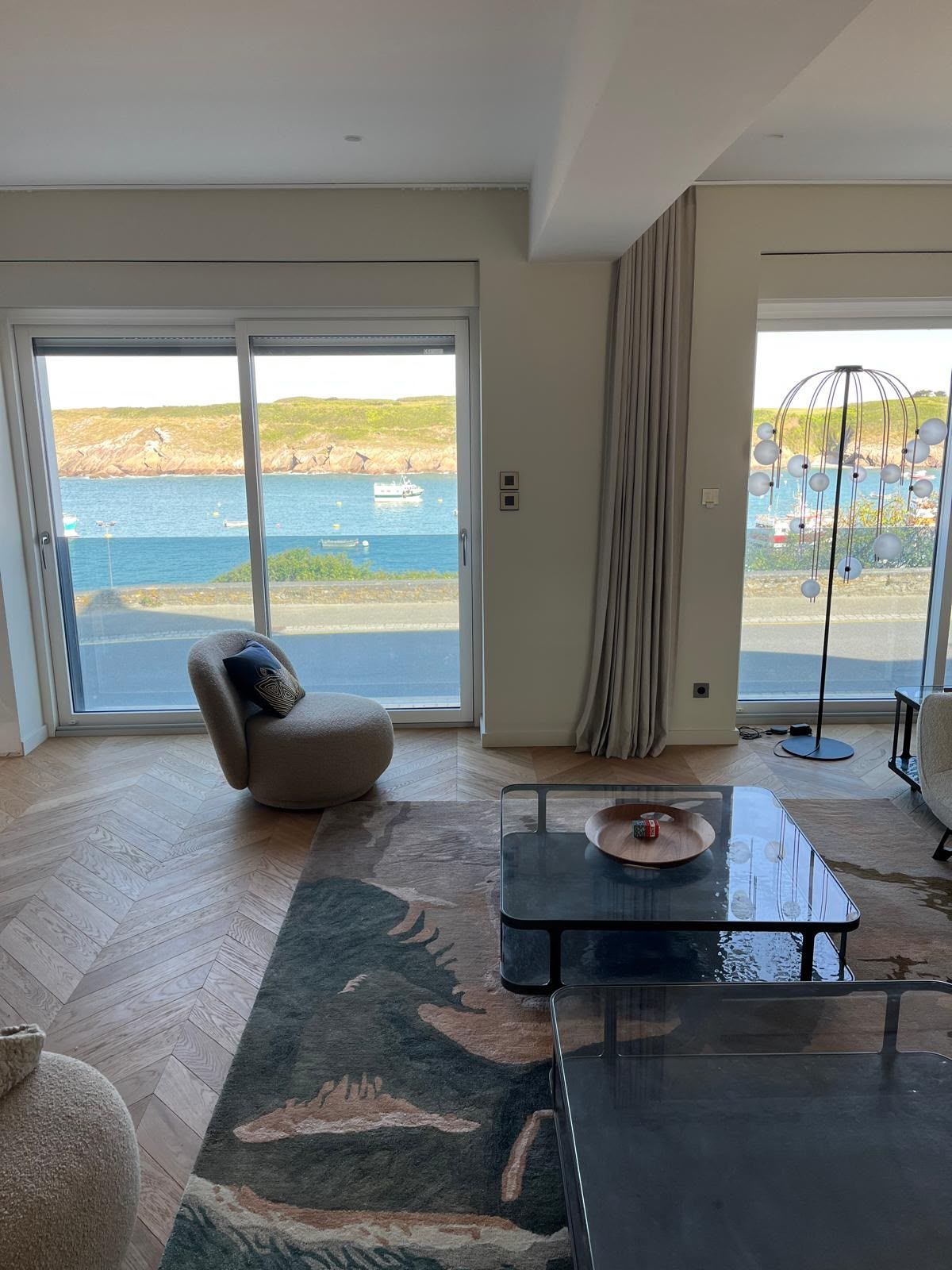 Salon lumineux avec vue sur l’océan, baie vitrée coulissante, tapis, table basse et fauteuil lounge.