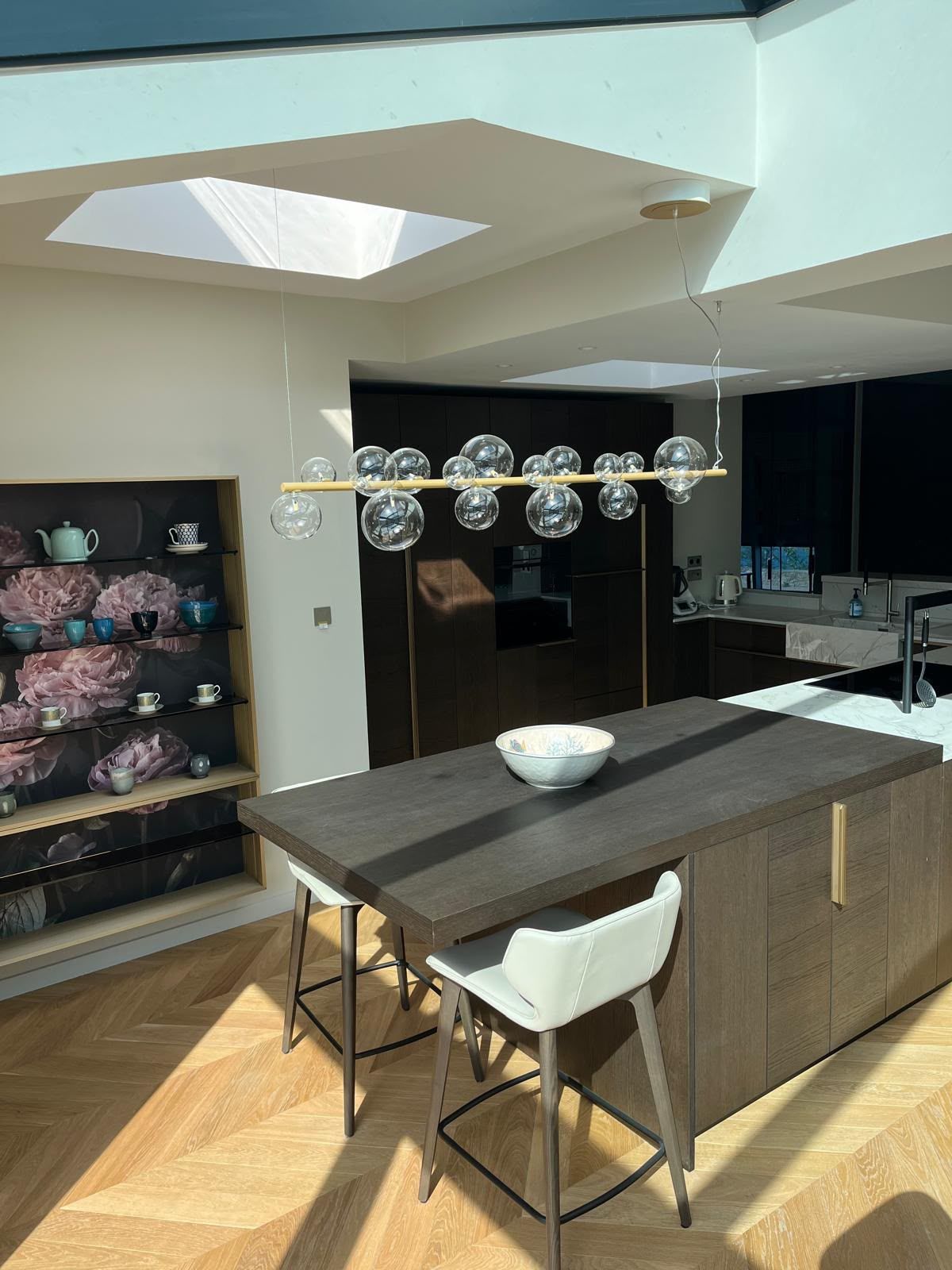 Cuisine moderne avec îlot central, suspensions, puits de lumière et étagères intégrées.