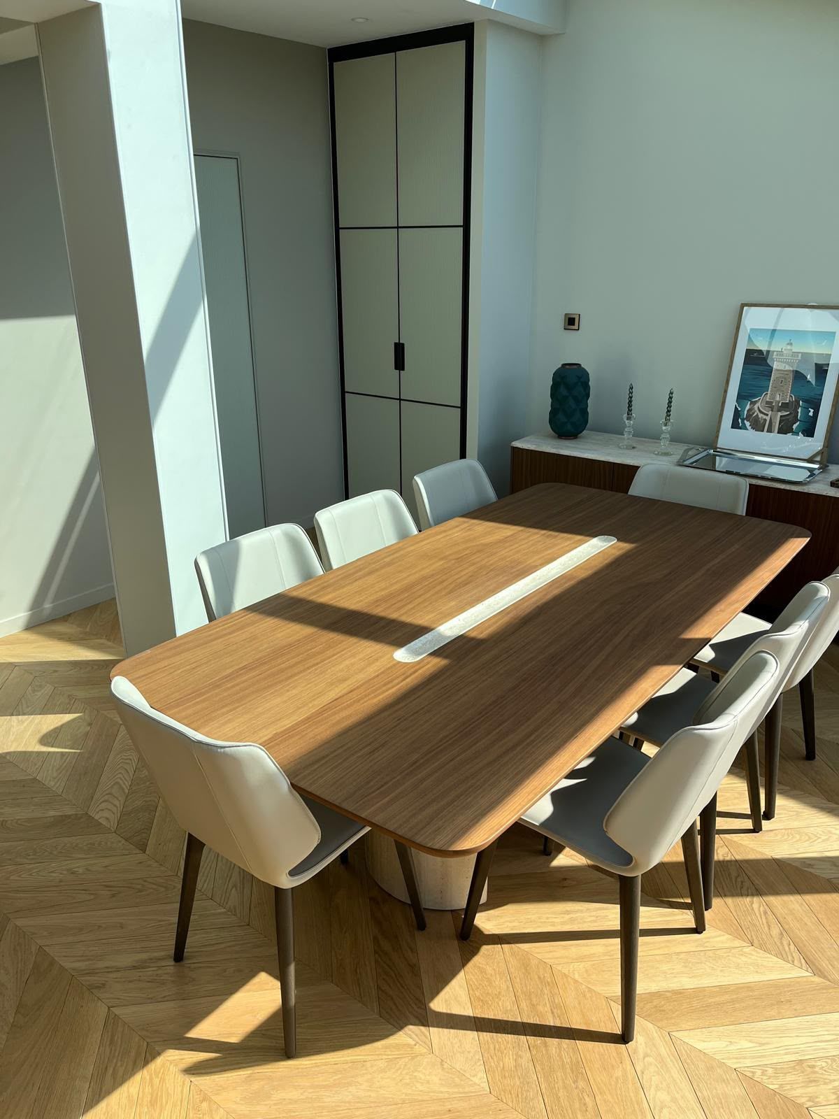 Salle à manger moderne avec une table en bois, des chaises blanches et la lumière du soleil qui baigne le sol