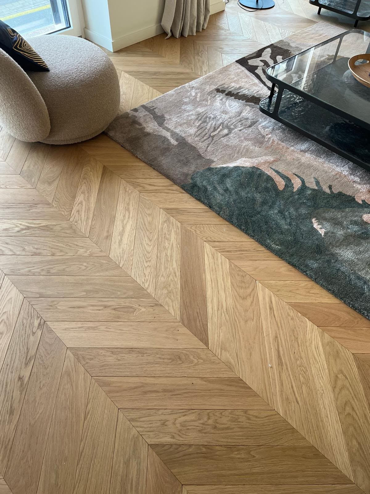 Parquet en chevrons à côté d’un tapis gris et d’une table basse en verre dans un salon moderne