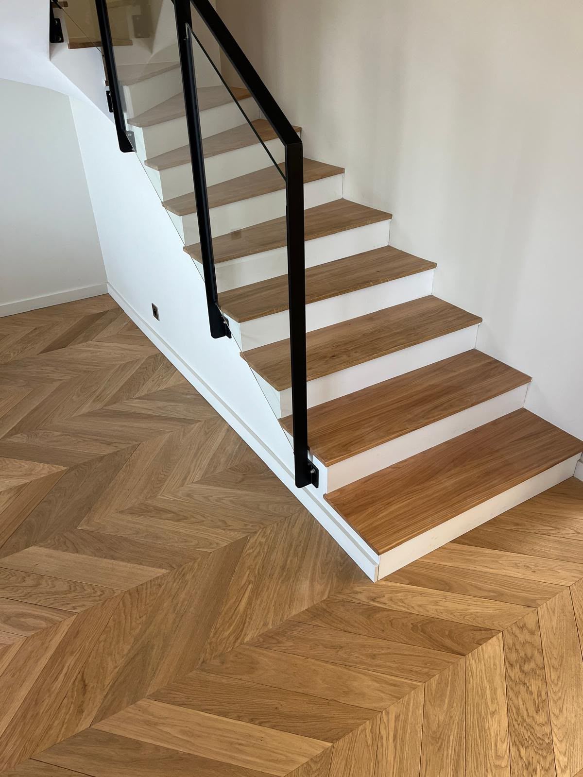 Escalier moderne avec une rampe noire et un parquet à chevrons dans un intérieur blanc