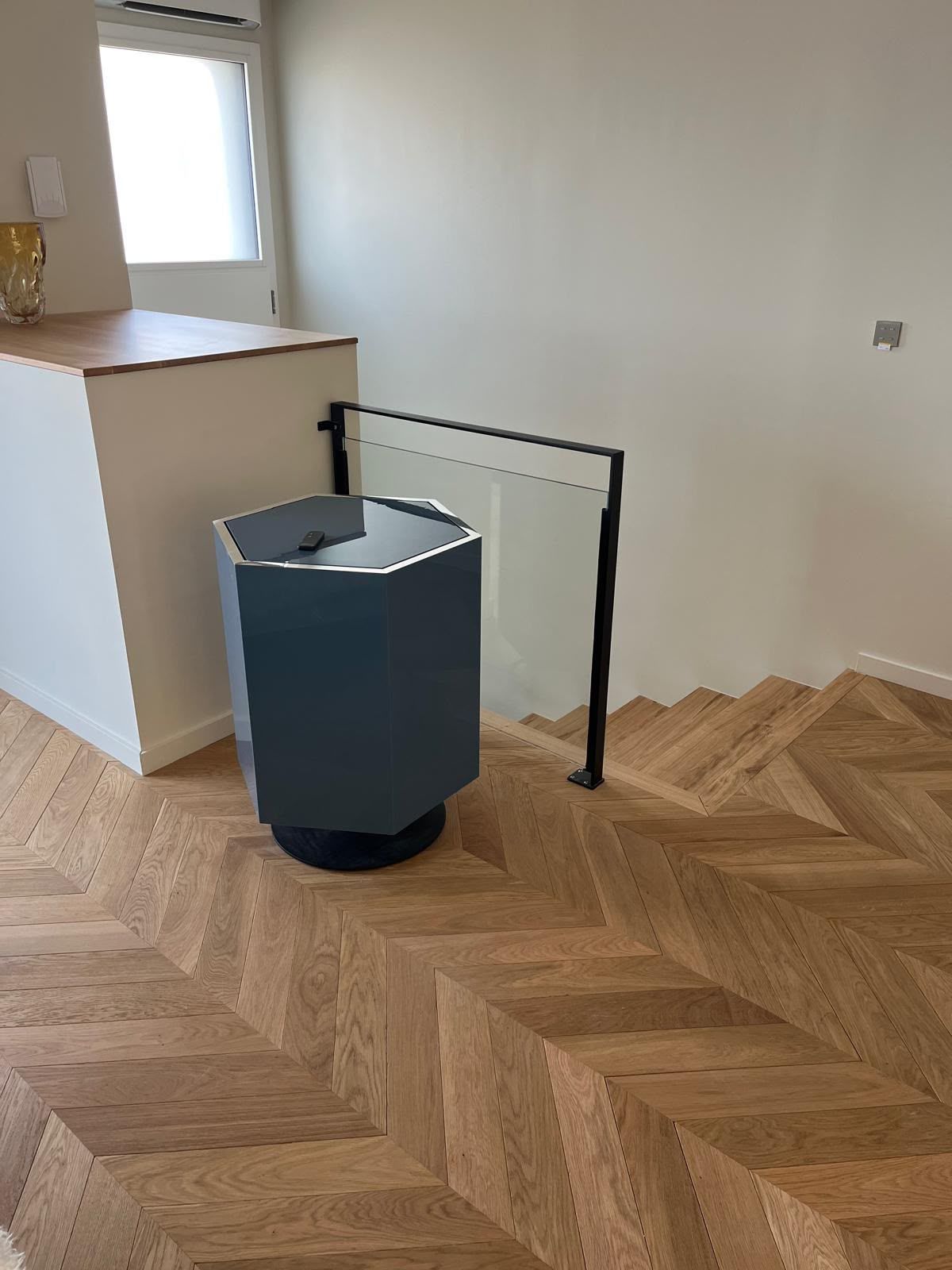 Pièce moderne avec un parquet en bois à chevrons, une poubelle grise et une barrière de sécurité noire près d’un comptoir.