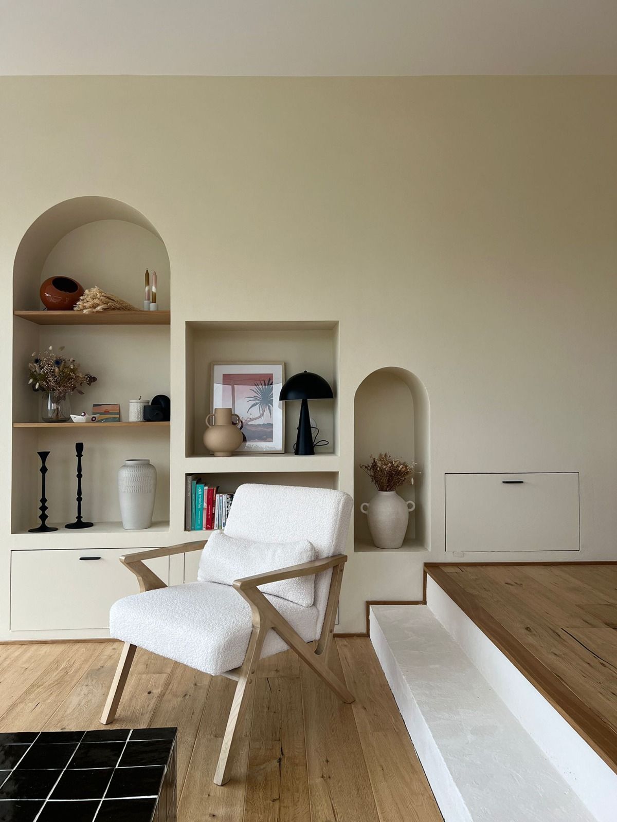 Salon minimaliste avec un fauteuil blanc, des étagères intégrées, des niches en arche et des marches en bois en estrade