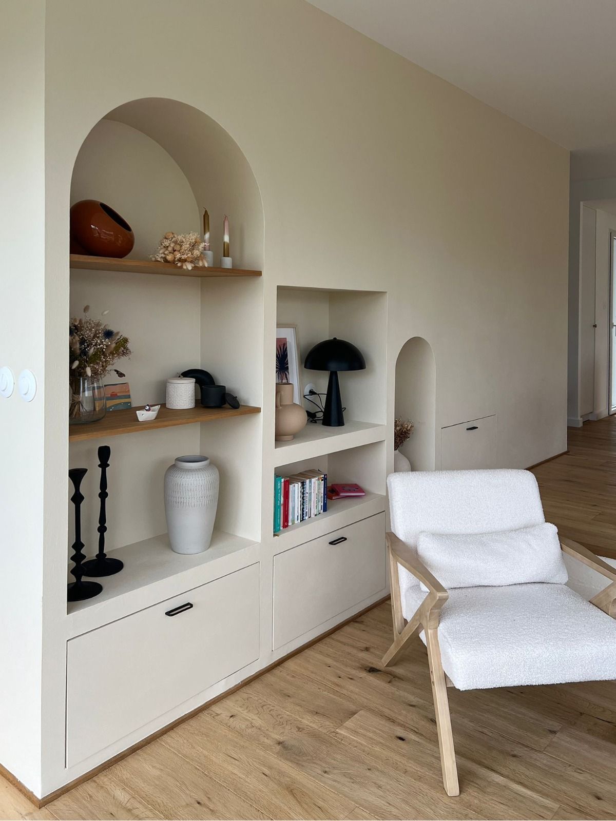 Étagères intégrées et décoration dans une pièce beige lumineuse avec un fauteuil blanc et un parquet en bois