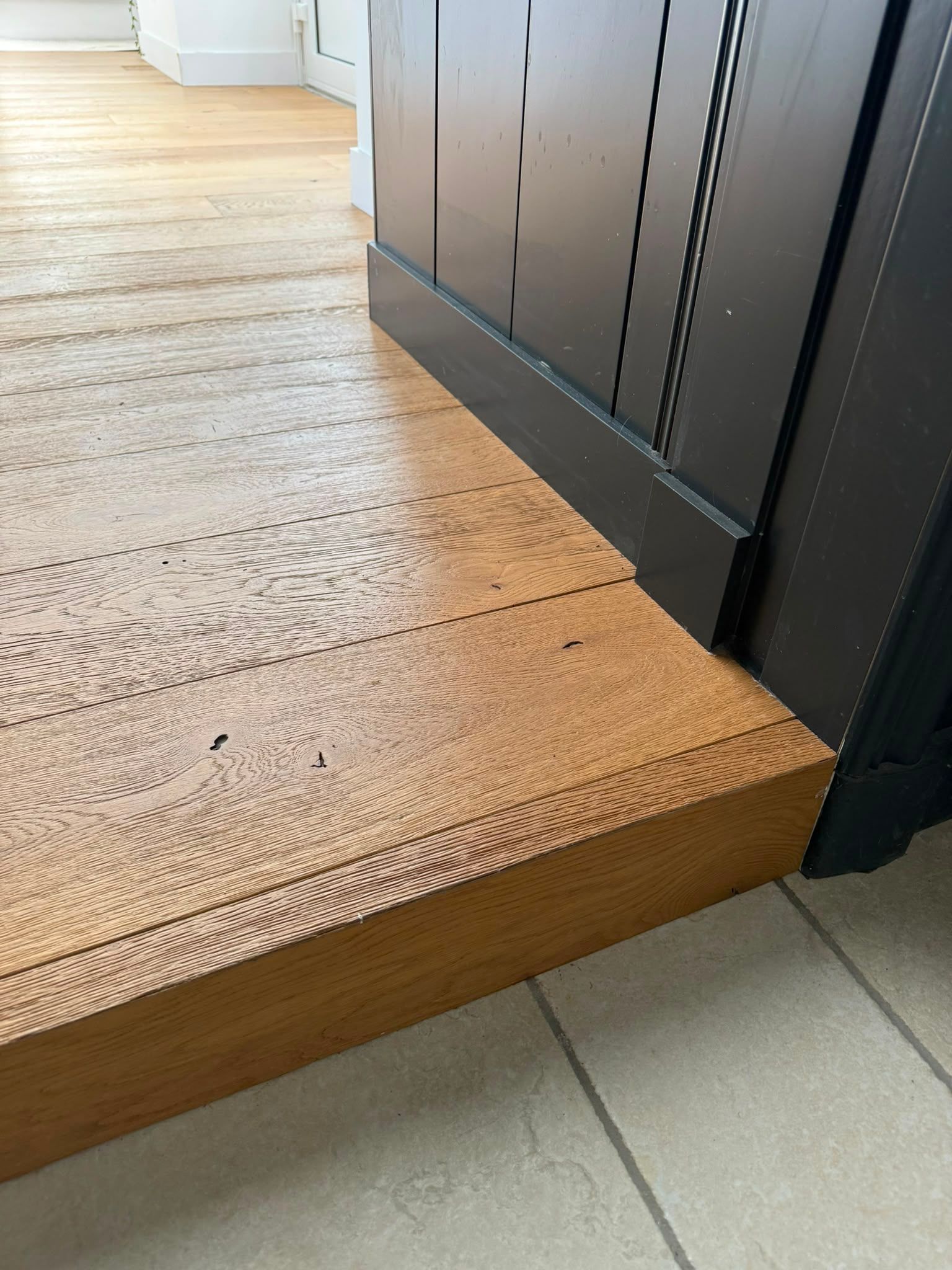 Seuil en bois au niveau d’un sol carrelé clair, à côté d’un meuble sombre ou d’un panneau de porte