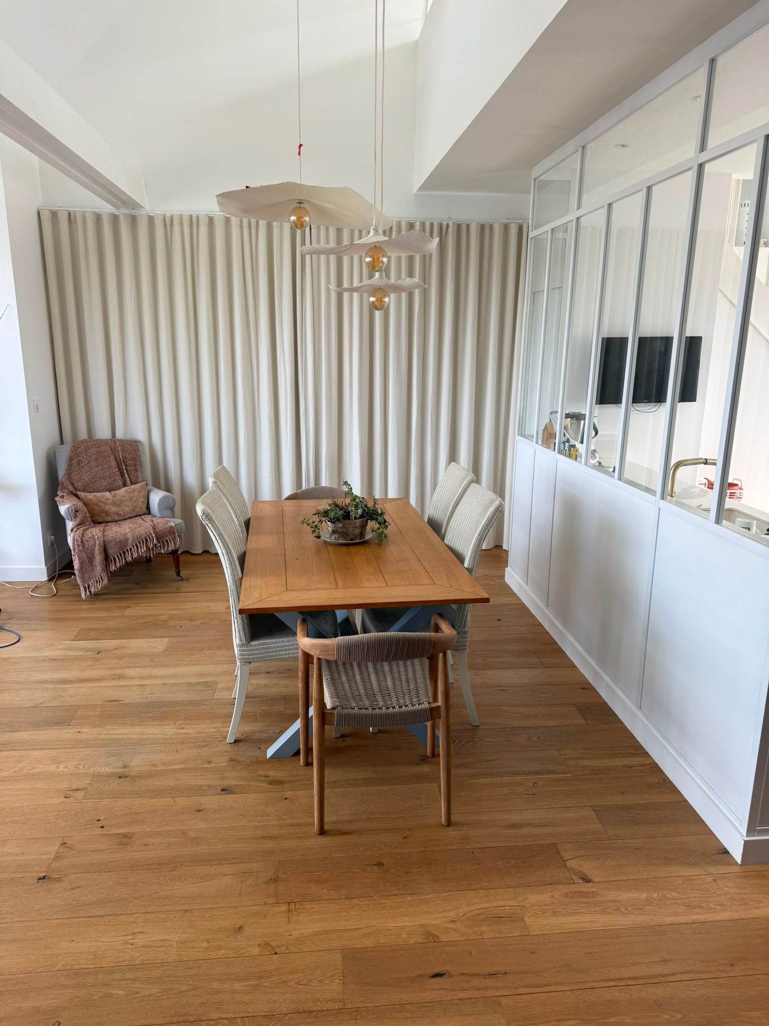 Salle à manger avec une table en bois, des chaises en rotin, des suspensions et de grands panneaux muraux miroir.