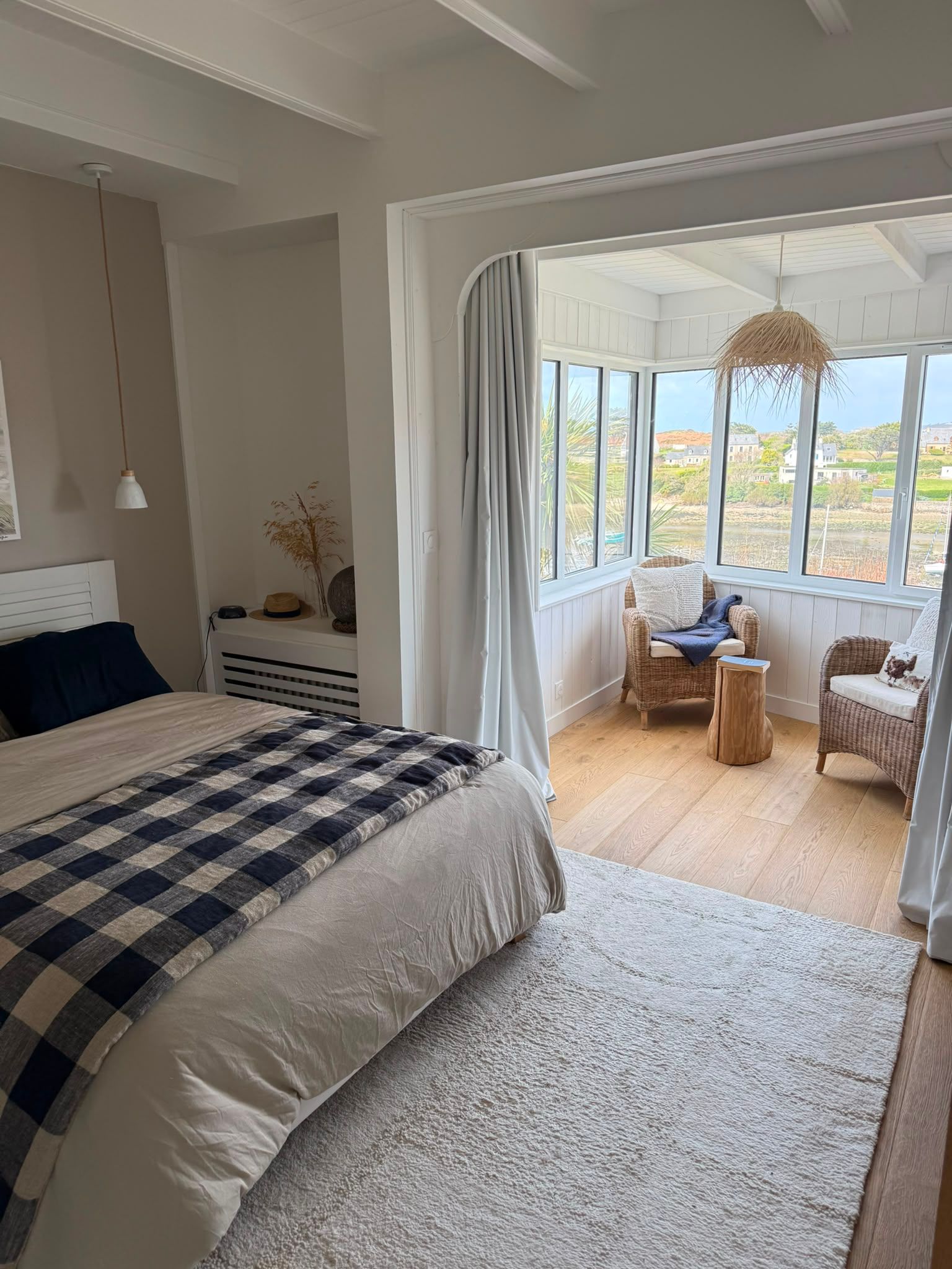 Chambre lumineuse donnant sur une véranda avec des fauteuils, une table et de grandes fenêtres offrant une vue pittoresque