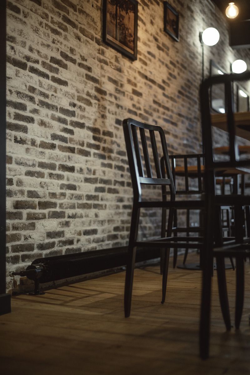 Intérieur de café tamisé avec un mur de briques, un parquet en bois et des chaises noires autour des tables
