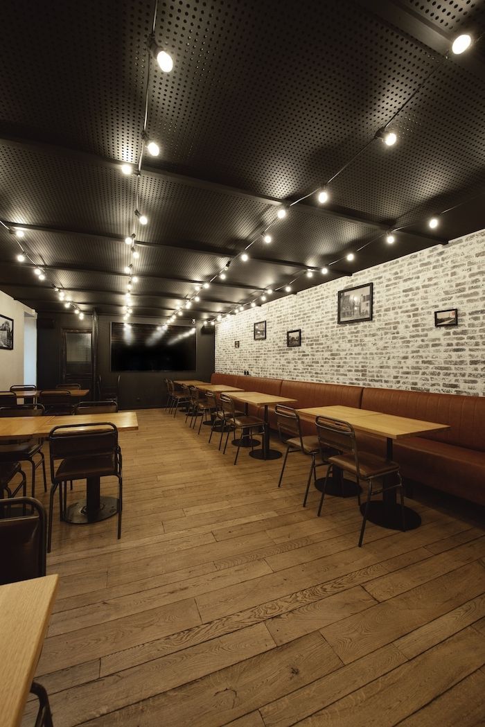 Intérieur vide d’un restaurant, avec des tables en bois, de longues banquettes et un éclairage chaleureux au plafond