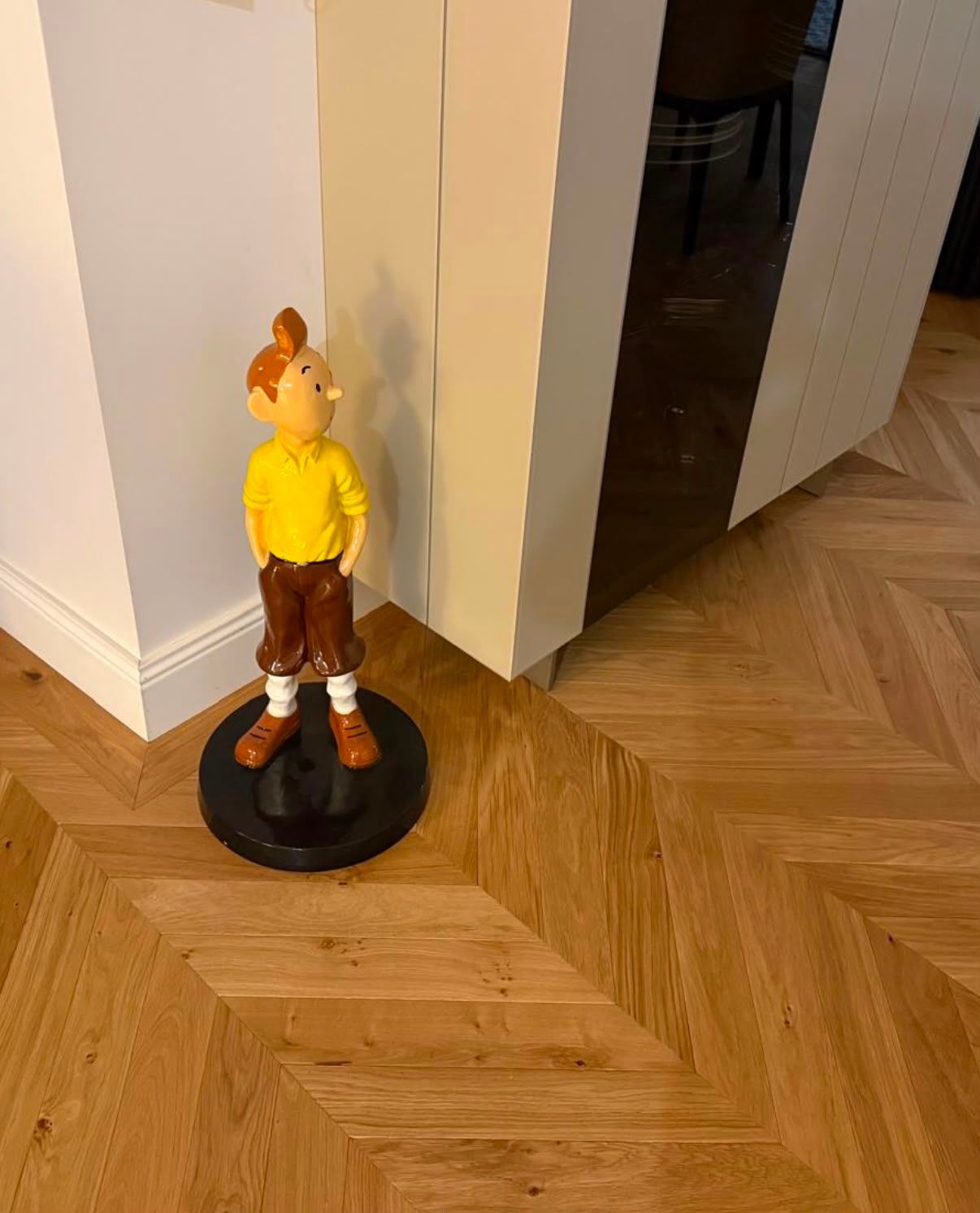 Figurine de Tintin sur un socle noir, à côté d’une porte ouverte dans une pièce au parquet en bois dur