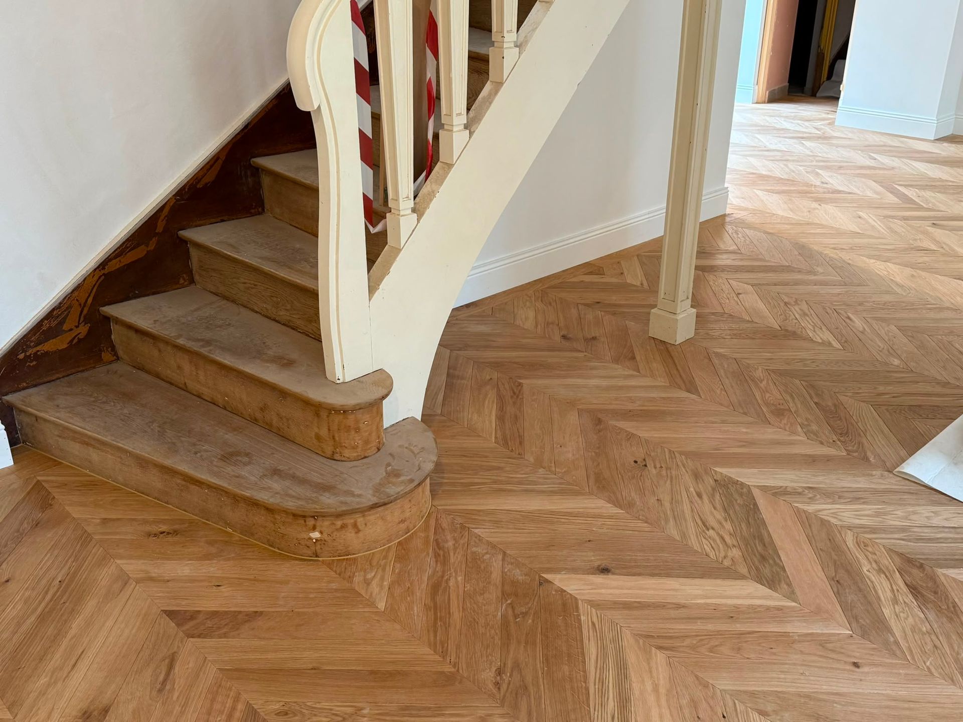 Escalier en bois avec une rampe blanche, à côté d’un parquet à chevrons dans un couloir