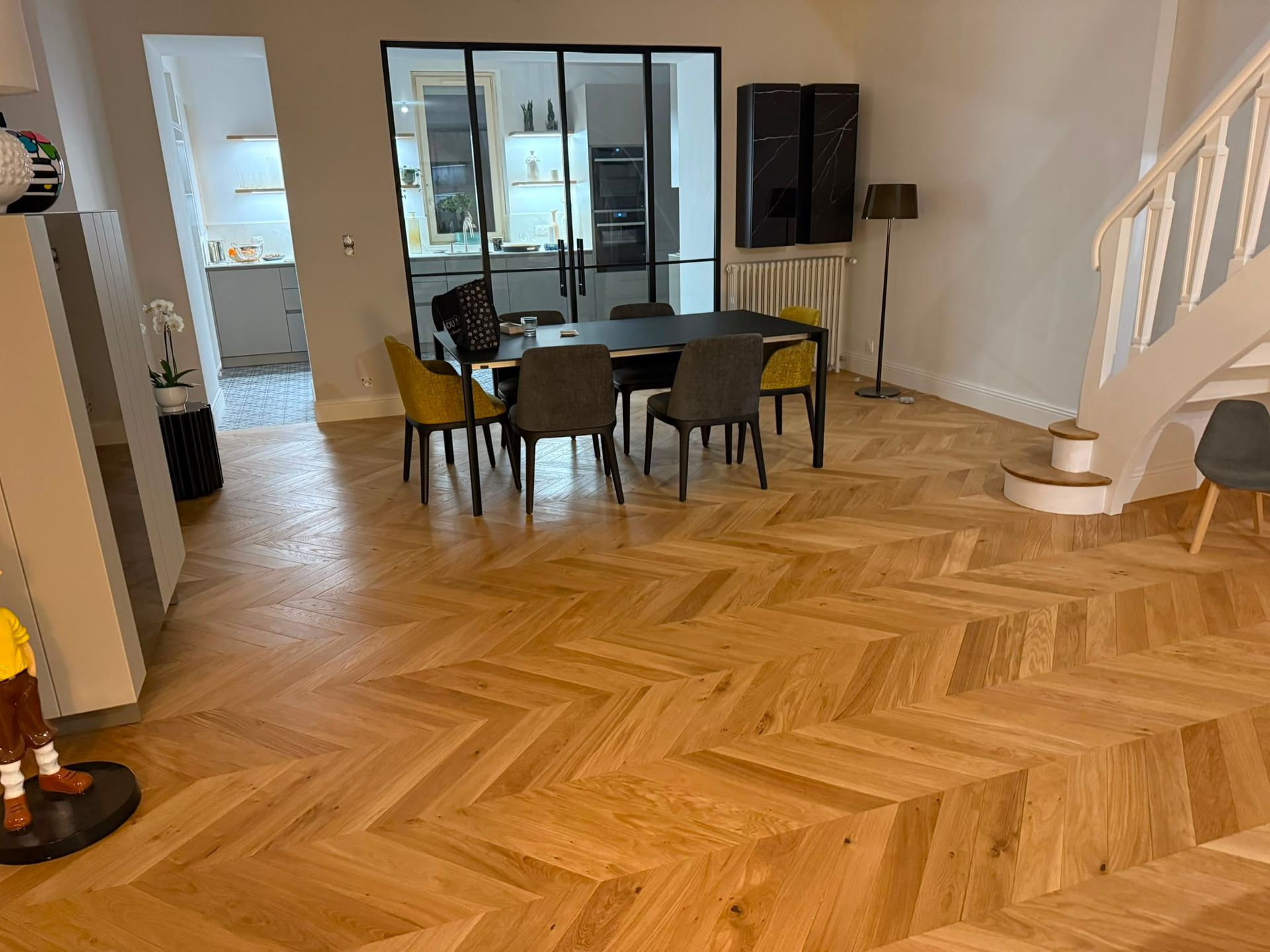Salle à manger moderne avec parquet en chevrons, table et chaises en verre, et escalier à droite