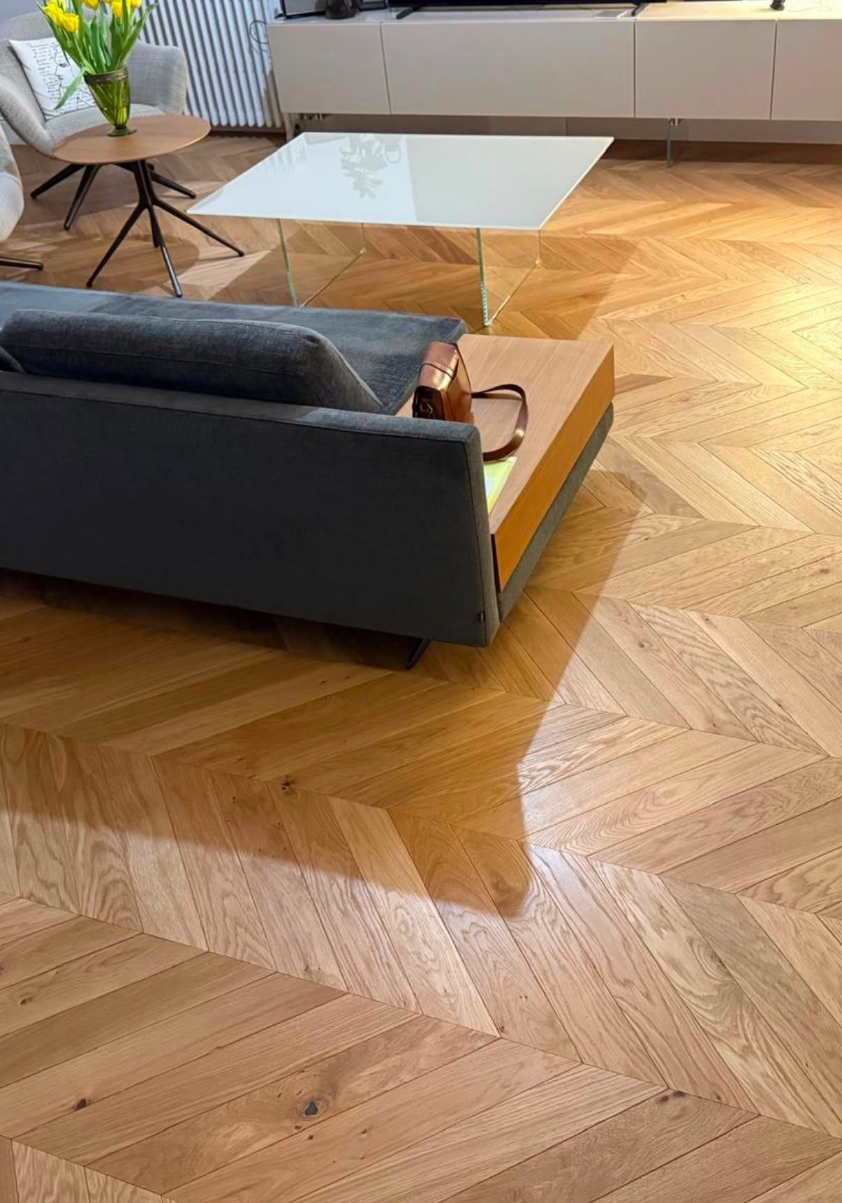 Salon moderne avec un canapé foncé, une table basse en verre et un parquet à chevrons