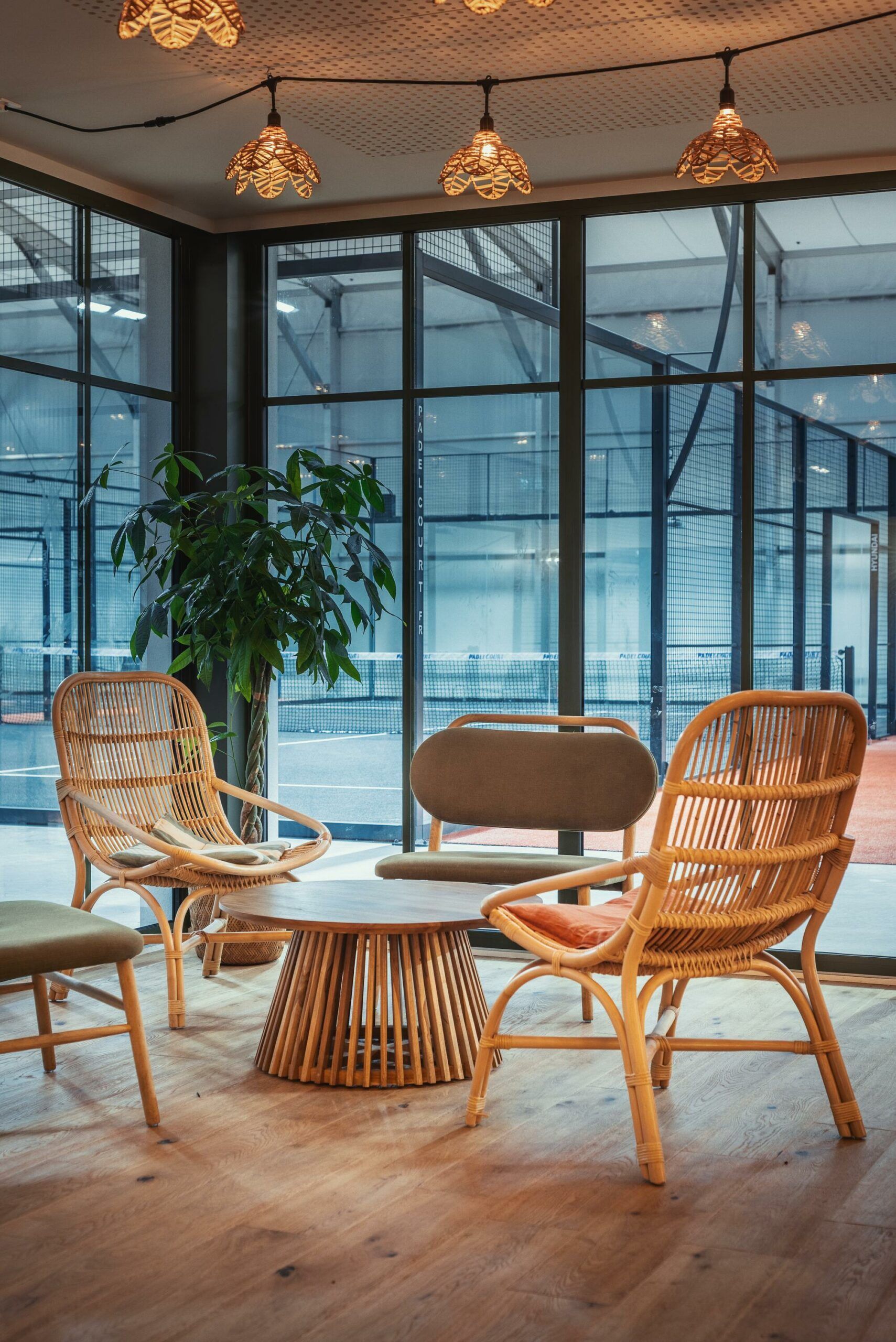 Salon chaleureux avec des fauteuils en osier, une table ronde et des suspensions près de grandes fenêtres