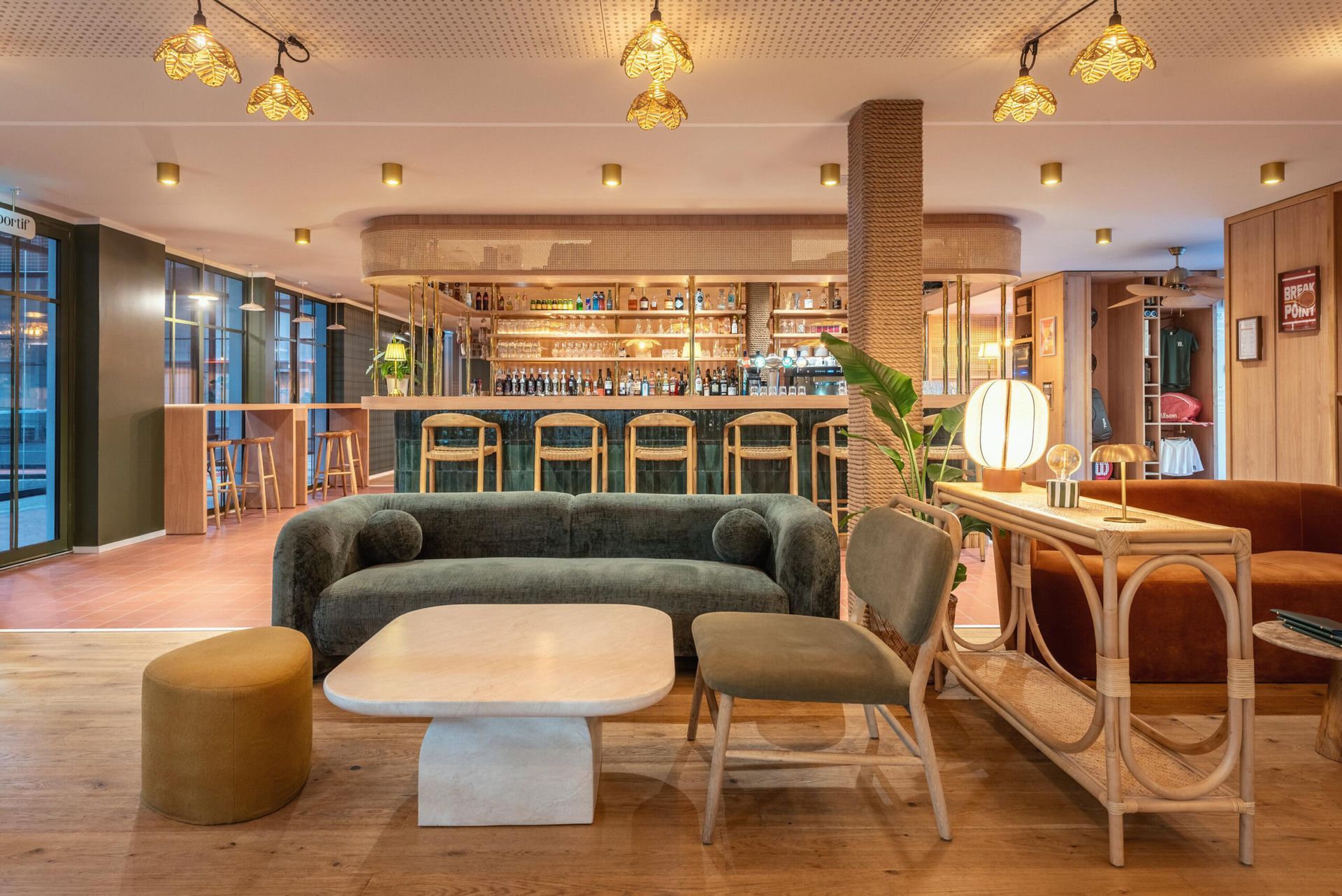 Salon élégant avec un canapé vert, une table basse en marbre et un espace bar éclairés par des suspensions chaleureuses