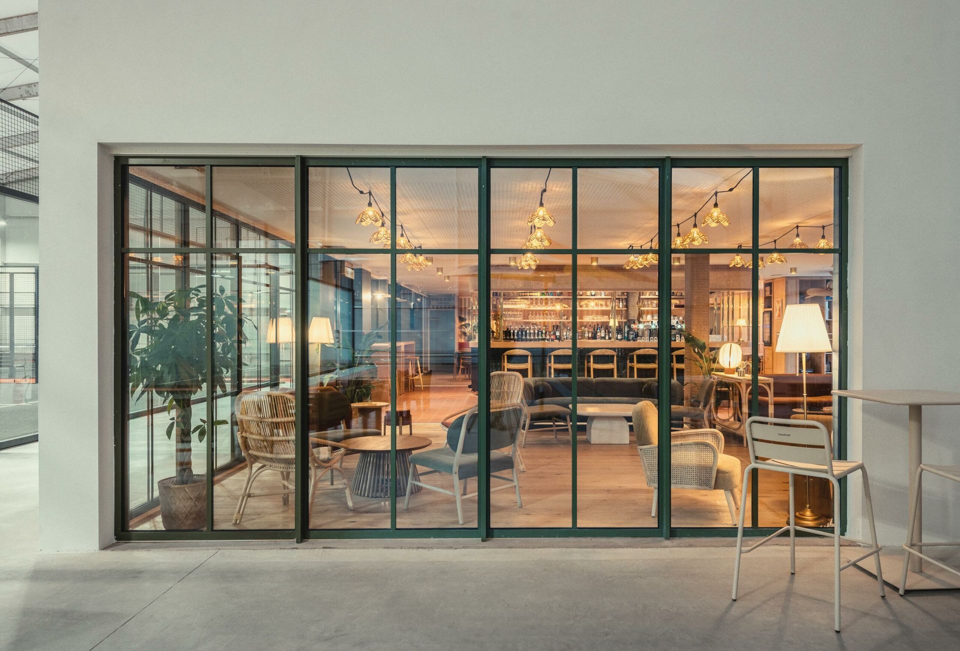 Café moderne aux parois vitrées, avec un éclairage chaleureux et des tables à l’intérieur, vu de l’extérieur.