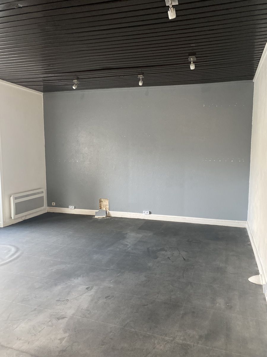 Pièce vide avec un mur d’accent gris, un sol noir et des luminaires au plafond à motifs sombres.