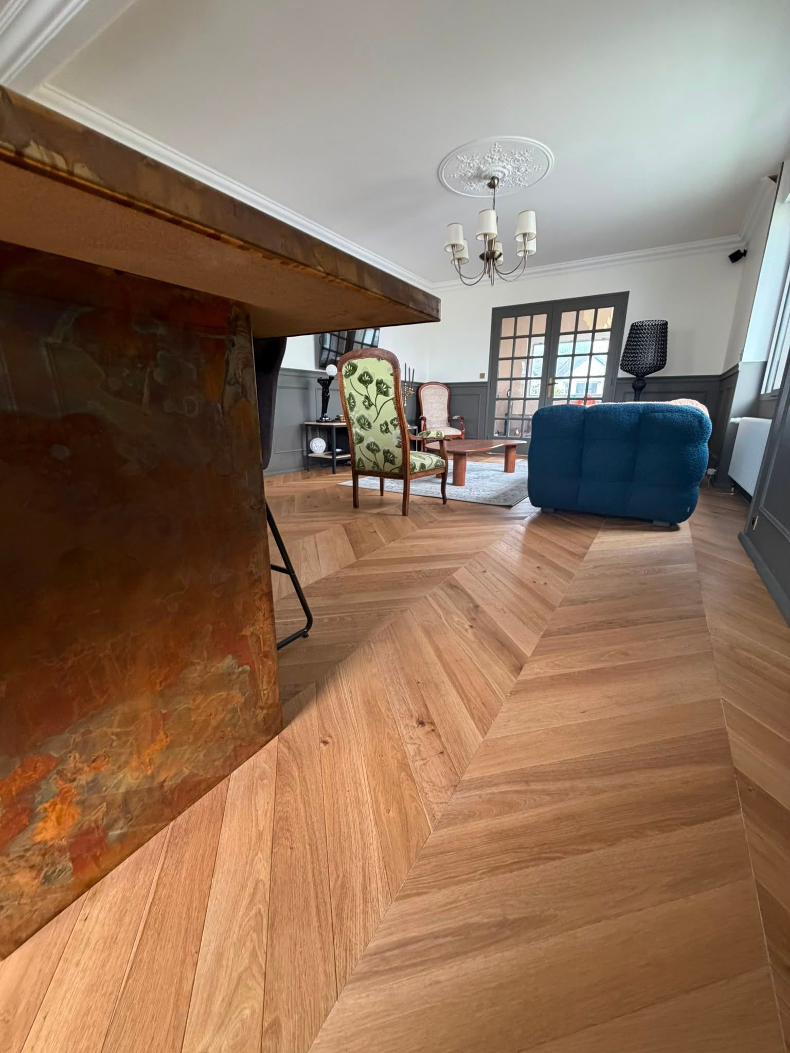 Salon avec parquet en chevrons, canapé bleu, table à manger et cheminée avec manteau visibles