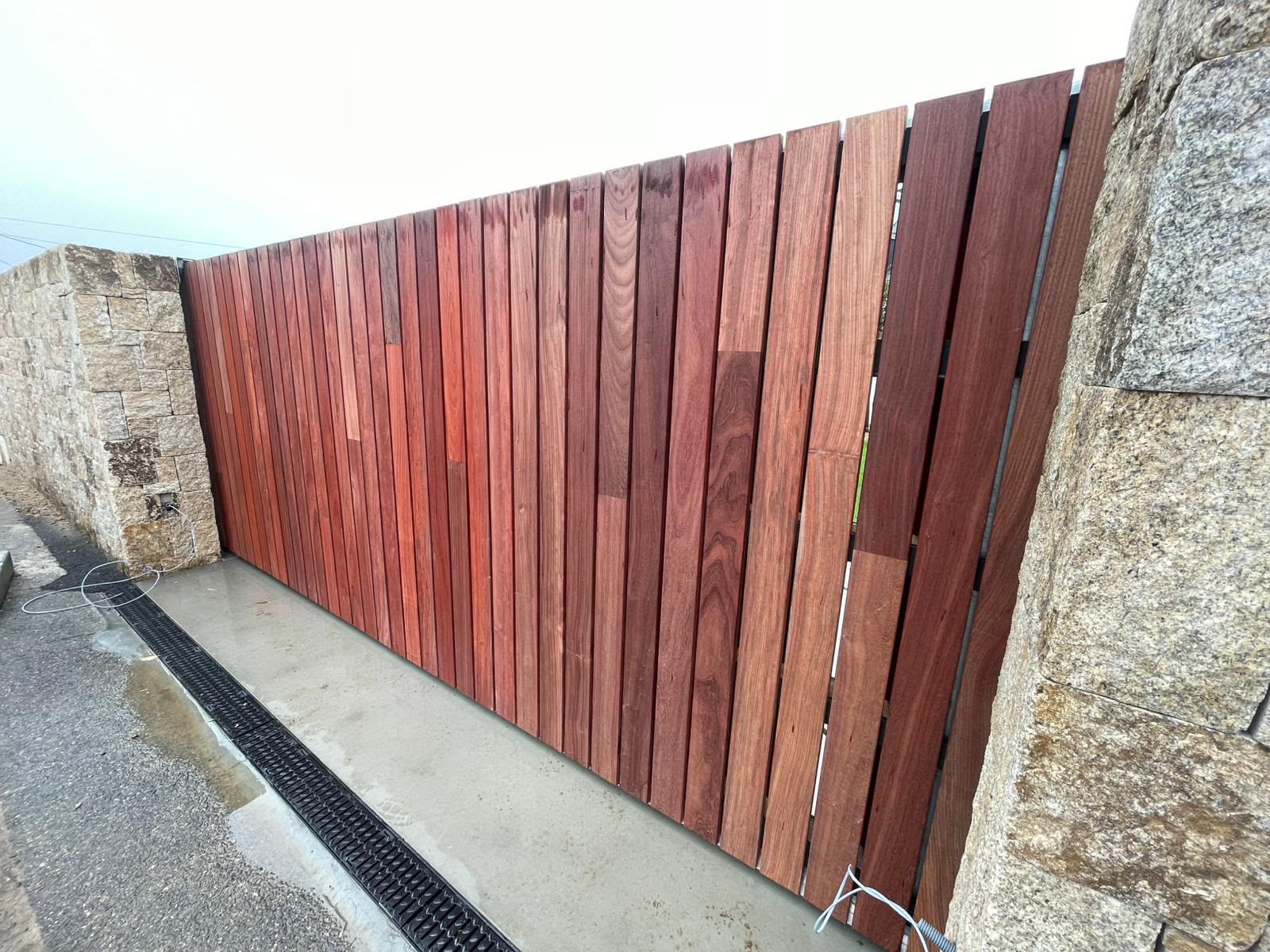 Clôture en lattes de bois rouge à côté d’une allée en béton et de murs en pierre